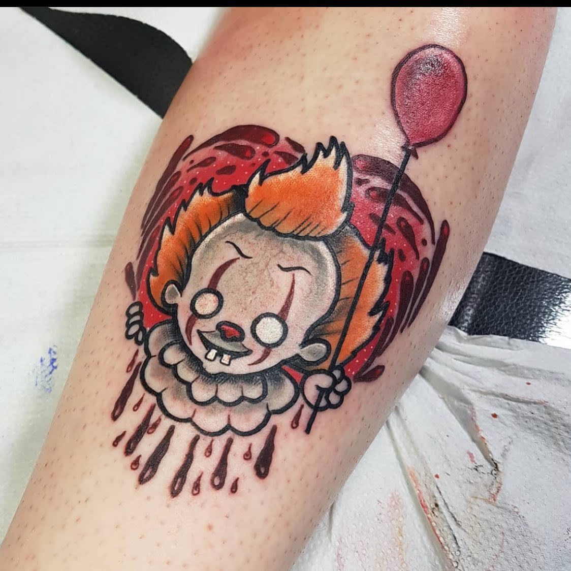 New school Pennywise tattoo on leg, featuring cartoonish design with a red balloon and drips